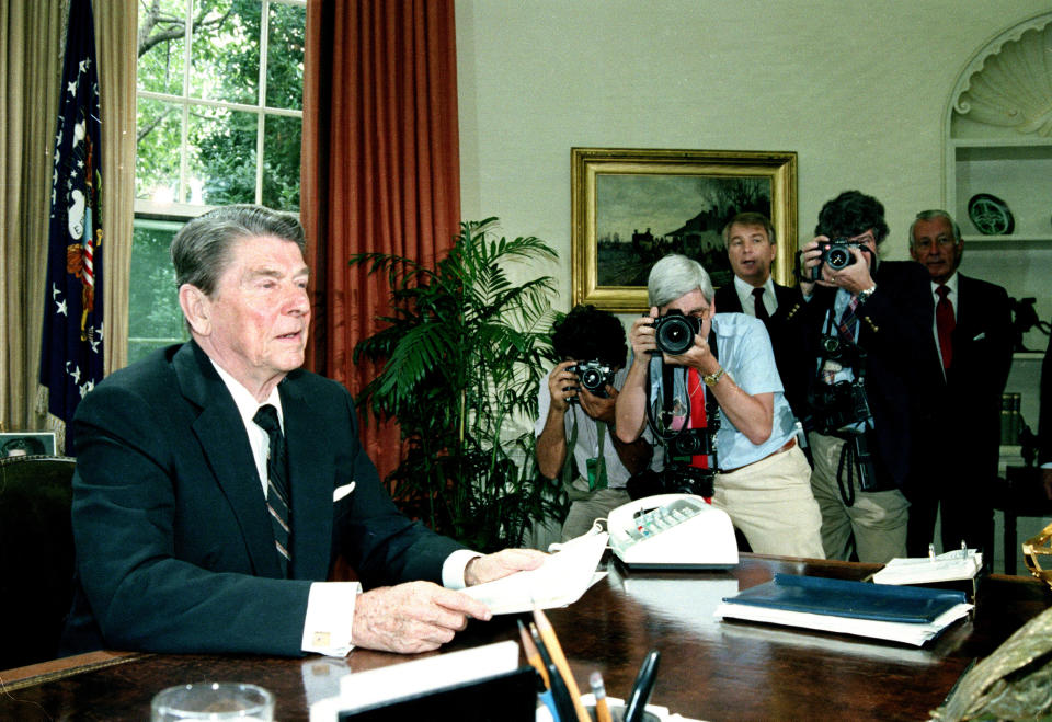 FILE - In this June 25, 1986 file photo, U.S. President Ronald Reagan appeals to the House of Representatives for their support in approving aid to Nicaraguan rebels in a televised speech from the Oval Office at the White House in Washington, D.C. White House spokesman Larry Speakes, third from right, and White House Chief of Staff Donald Regan, right, look on from behind photographers. In the 1980s, the Reagan administration backed anti-Communist Contra forces against Nicaragua’s Sandinista government and backed the Salvadoran government against leftist FMLN rebels. (AP Photo/Barry Thumma, File)