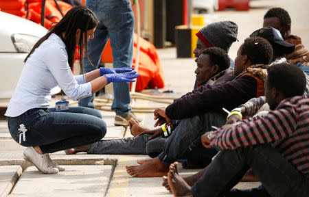 A police immigration officer talks to migrants sitting on the ground as they wait for police buses to take them away to camps, after they disembarked from an Armed Forces of Malta patrol boat at its base in Marsamxett Harbour, Valletta, Malta May 25, 2019. REUTERS/Darrin Zammit Lupi