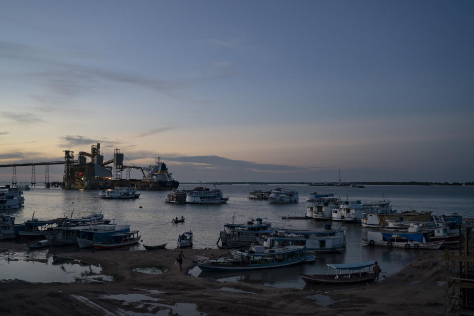 This Nov. 18, 2019 photo shows boats at dusk in a port at Santarem, Para state, Brazil, at the confluence of the Tapajos and Amazon rivers. The grain export terminal, top left, loads ships with grains, which are then dispatched across the world, largely to China. (AP Photo/Leo Correa)