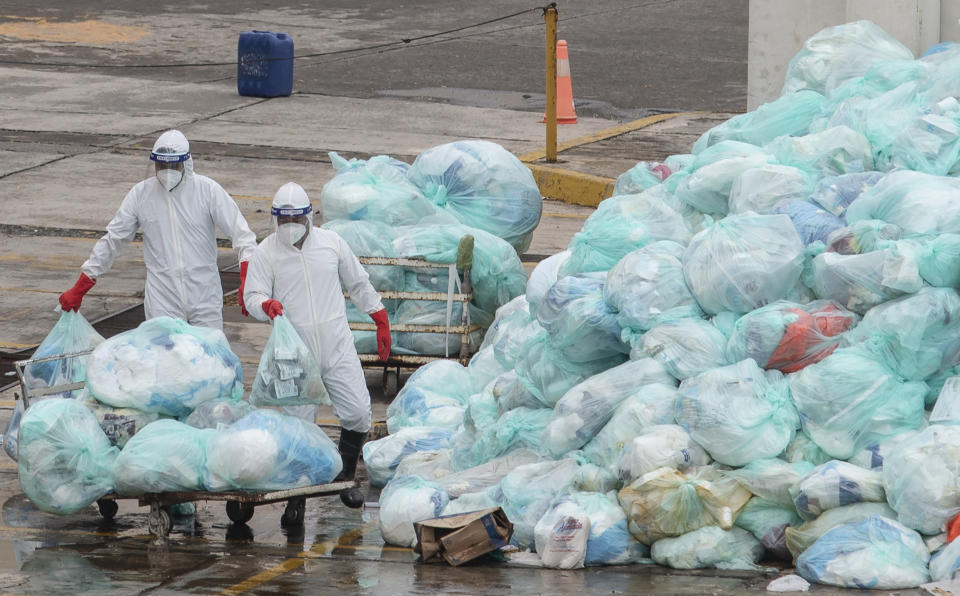 Medical workers using protective equipment dispose of trash bags containing hazardous biological waste into a large pile outside the Hospital del Instituto Mexicano del Seguro Social, which treats patients with COVID-19 in Veracruz, Mexico, Wednesday, Aug. 12, 2020. Improper disposal of medical waste has become an increasing problem in Mexico amid the pandemic. (AP Photo/Felix Marquez)