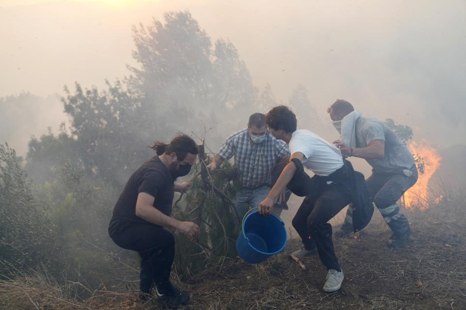 FILE - Local residents use buckets with water to try to slow down flames approaching their houses in Alcabideche, outside Lisbon. Tuesday, July 25, 2023. As wildfires become more common in Portugal, six children and young adults felt empowered to take 32 European governments to court on Wednesday, Sept. 27, 2023, for what they say is a failure to adequately address human-caused climate change in a violation of their human rights. (AP Photo/Armando Franca, File)