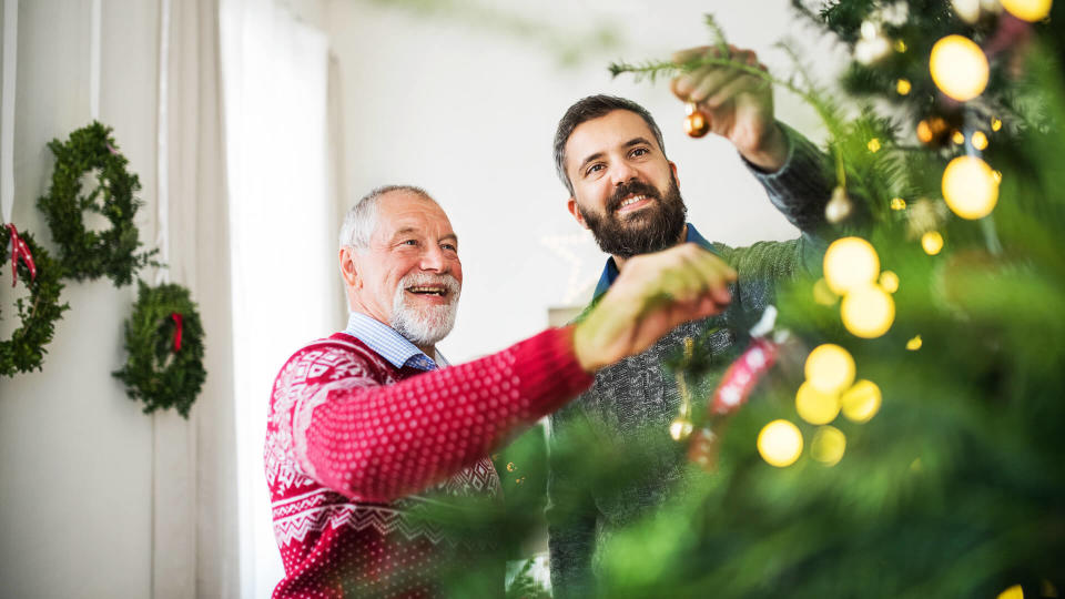 A happy senior father and adult son decorating a Christmas tree at home.