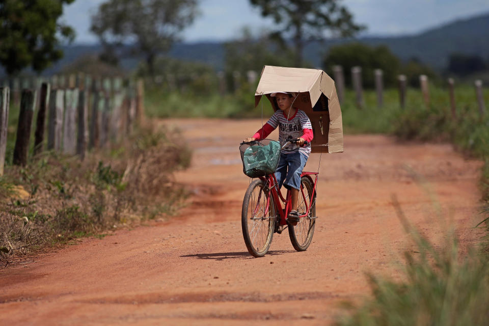In this March 4, 2014 photo, Rafael Freire de Andrade, 8, who suffers from a rare inherited skin disease known as xeroderma pigmentosum, or "XP," rides his bike that has a cardboard box to shade himself from th sun, in the Araras community of Brazil's Goias state. Those with the disease are extremely sensitive to ultraviolet rays from sunlight and highly susceptible to skin cancers. That’s a particularly vexing burden in Araras, a tropical farming community where outdoor work is vital for survival. (AP Photo/Eraldo Peres)