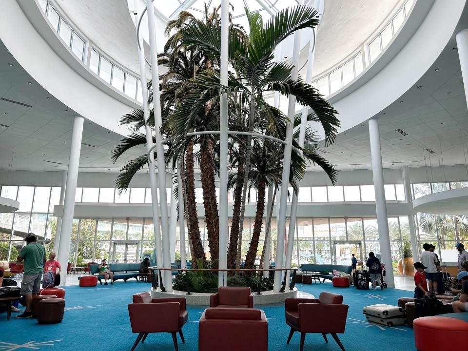 A hotel lobby with large palm trees in the middle. There is blue carpeting and red seats.