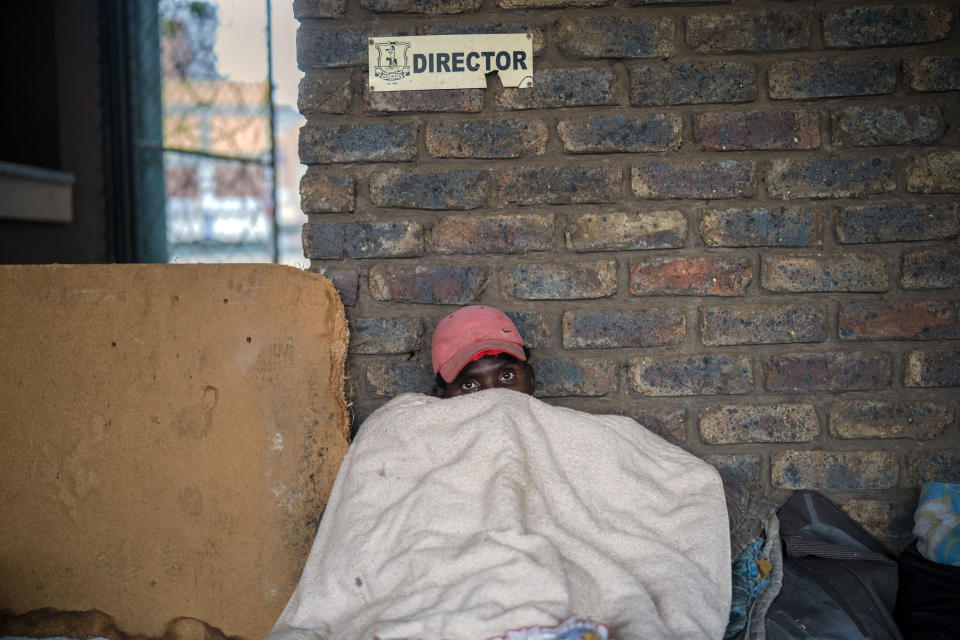 Andrew rests under a blanket as he and other homeless people rest at the Caledonian stadium downtown Pretoria, South Africa, Thursday April 2, 2020, after being rounded up by police in an effort to enforce a 21 days lockdown to control the spread of the coronavirus. Many of them being addicted, they are receiving methadone syrup from a local NGO, and were complaining about the lack of sanitizer and soap. The new coronavirus causes mild or moderate symptoms for most people, but for some, especially older adults and people with existing health problems, it can cause more severe illness or death.(AP Photo/Jerome Delay)