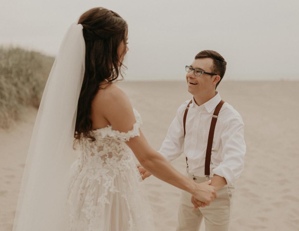 A bride and her brother hold hands on a beach.