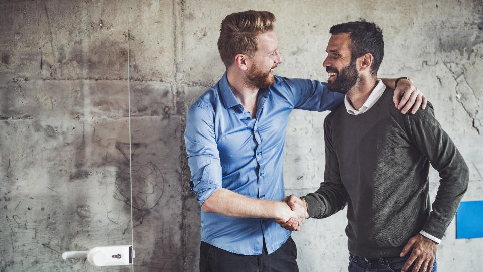 Young happy businessmen talking while shaking hands in the office.