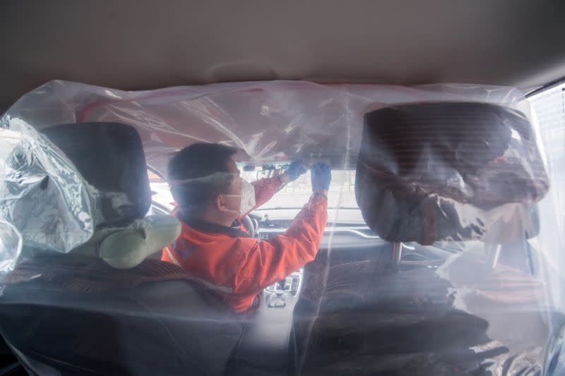 Worker installs plastic film to separate the front seats from the back, inside a vehicle for a car-hailing service as the country is hit by an outbreak of the novel coronavirus, in Taiyuan