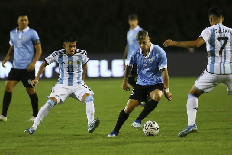 Valentín Rodríguez lleva la pelota entre Claudio Echeverri y Pablo Solari, que colaboran en la recuperación; un primer tiempo muy intenso en Venezuela.