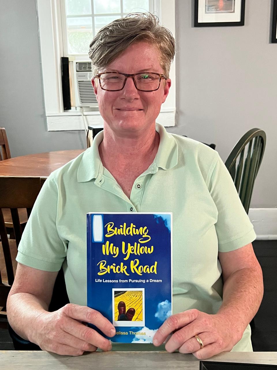 Melissa Thomas shows off a copy of her book "Building My Yellow Brick Road," which details her dream to meet Elton John.