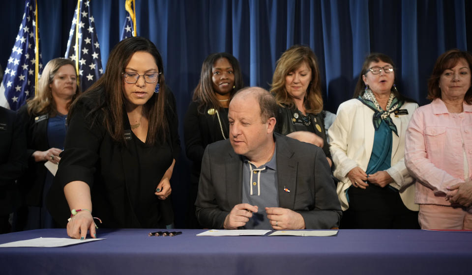 FILE - Colorado State Sen. Julie Gonzales, front left, confers with Colorado Gov. Jared Polis before he signs the first of three bills that enshrine protections for abortion and gender-affirming care procedures and medications during a ceremony with bill sponsors and supporters, April 14, 2023, in the State Capitol in Denver. The owner of a Catholic clinic challenging Colorado's new ban on unproven treatments to reverse medication abortions has testified that the state's pledge not to enforce it for now was not enough to protect her staff and patients. (AP Photo/David Zalubowski,File)