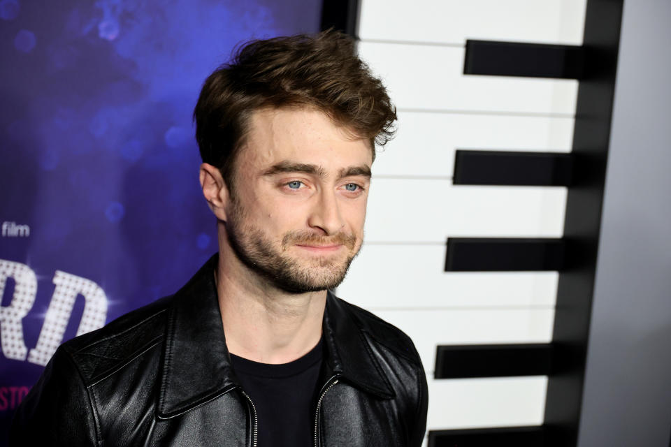 Daniel Radcliffe in a leather jacket at a red carpet event with a piano key backdrop