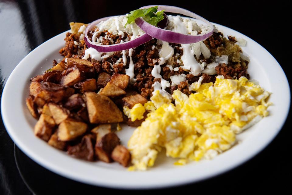 Chilaquiles, deep fried tortillas soaked in homemade green sauce made with tomatillos, topped with chorizo, sour cream, Queso Fresco and onion with scrambled eggs and potatoes on the side.