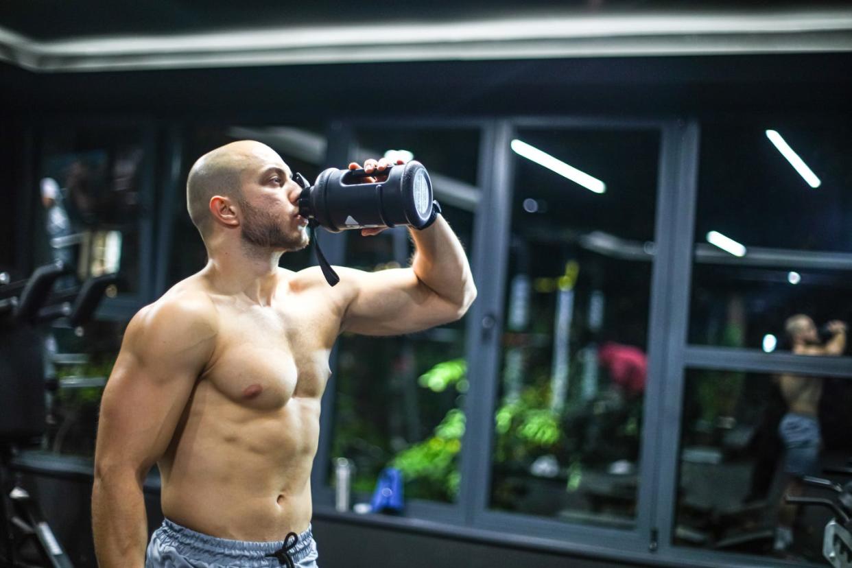 muscular men drink his nutritional supplement in gym