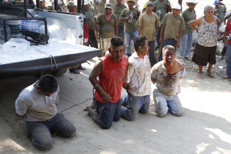 Members of the community police stand next to four men that were detained after they allegedly participated in an ambush against the community policemen near the town of La Concepcion, Mexico, Friday, April 4, 2014. The vigilante force was set-up by affected communities who created the Council of Communal Land Owners and Communities Against the Construction of La Parota Dam (CECOP), opposed to the construction of the La Parota hydroelectric dam. Two vigilantes were injured and one died. At least four suspects were later detained. (AP Photo/Bernandino Hernandez)