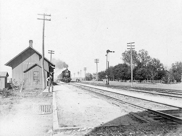 This photograph taken between the 1880s and 1890s shows a steam locomotive approaching the Atchison, Topeka and Santa Fe Railway Company depot in Clements, Kansas. In the foreground a man can be seen standing on the platform.