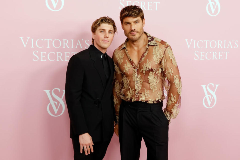 Lukas Gage in a suit and Chris Appleton in a sheer, floral-patterned shirt and black pants pose together at a Victoria's Secret event