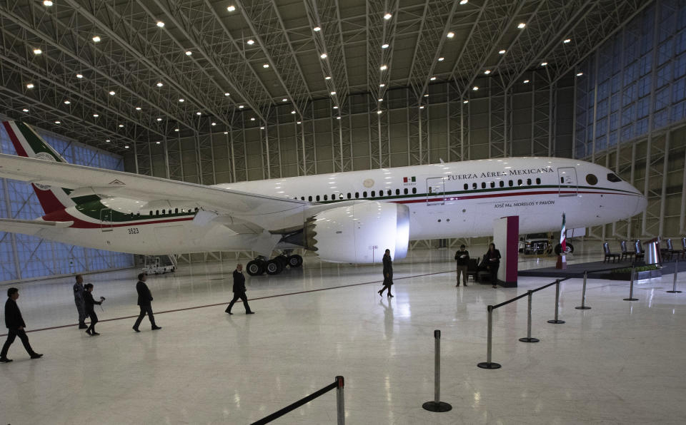 FILE - In this July 27, 2020 file photo, Mexican President Andres Manuel Lopez Obrador, center left, waves to the press as he arrives to give his daily, morning press conference in front of the former presidential plane at Benito Juarez International Airport in Mexico City. López Obrador’s quixotic bid to sell off the presidential jet has now stretched into its third year in 2021, with no sign of a buyer in sight. (AP Photo/Marco Ugarte, File)