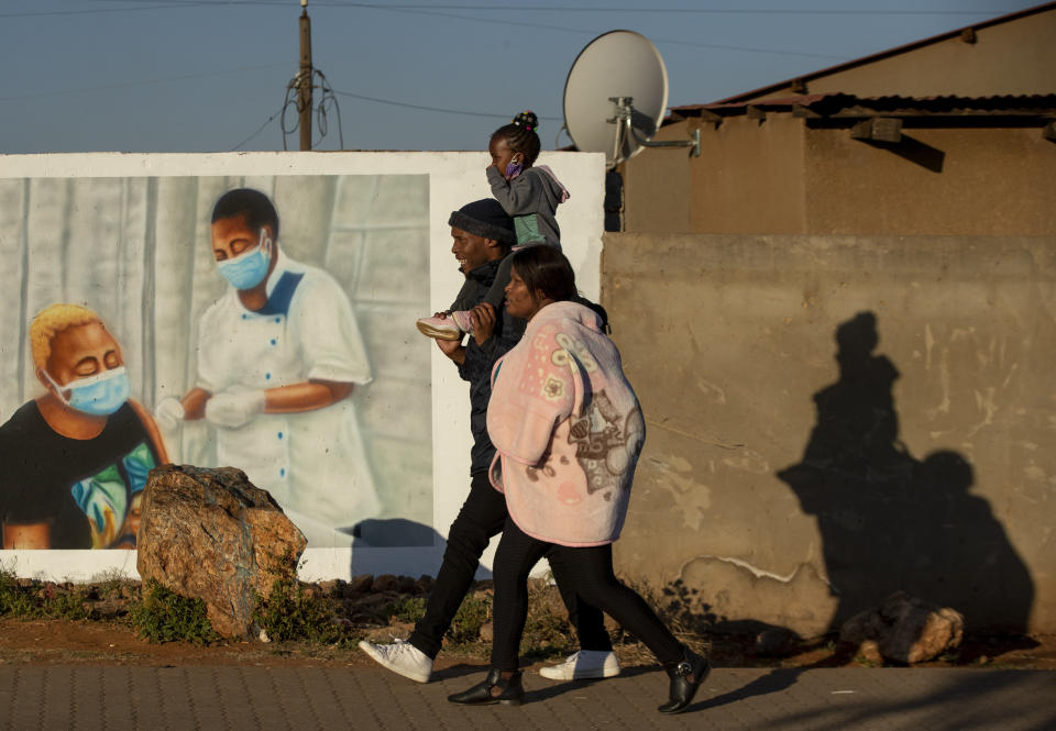 FILE - In this June 23, 2021, file photo, a family walks past a mural promoting vaccination for COVID-19 in Duduza township, east of Johannesburg, South Africa. New infections in South Africa rose to record levels in recent days, part of a rapid rise across the continent, and experts say the surge here has not yet peaked. South Africa reimposed several restrictions, and its vaccination drive is finding its feet after several stumbles. But even as the campaign gathers pace, experts say it's too late to reduce the deadly impact of the current spike. (AP Photo/Themba Hadebe, File)