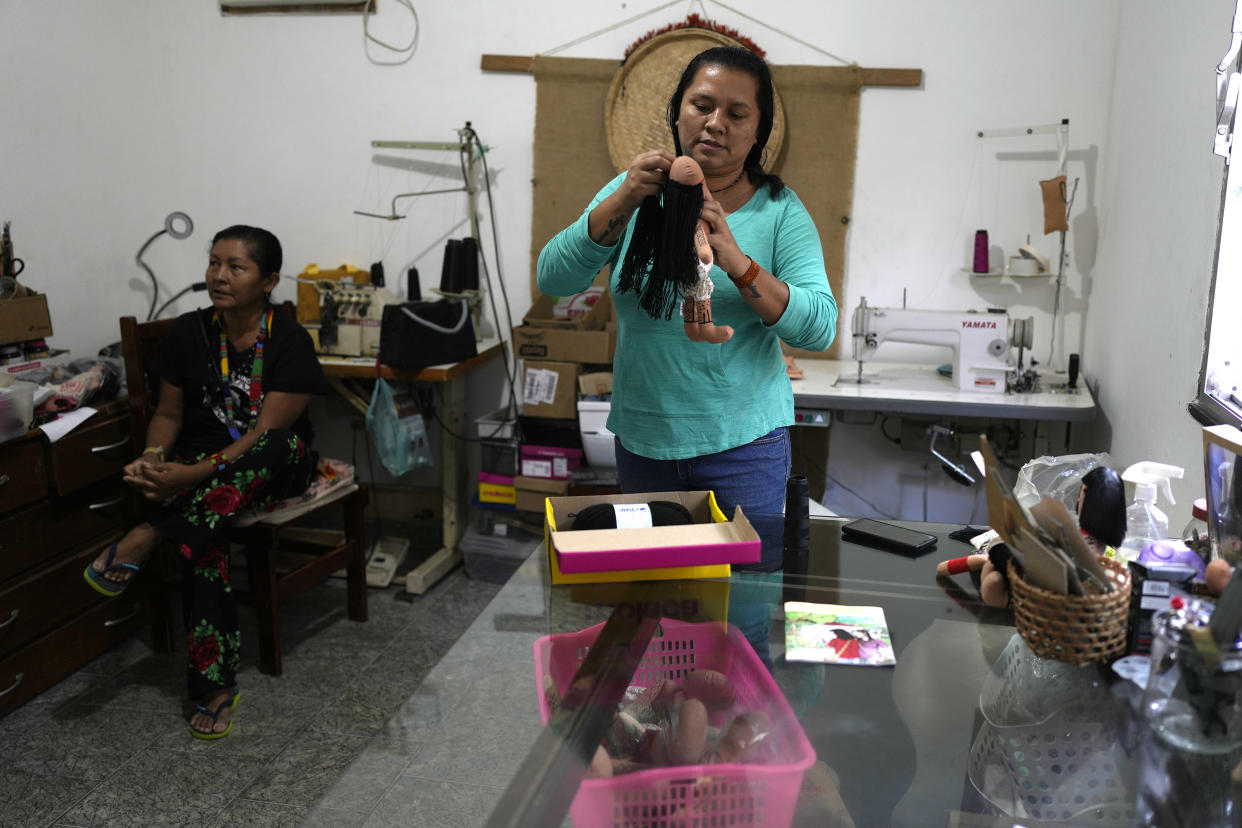 Atyna Pora, of Brazil's Anambe indigenous group, adds black yarn hair to an indigenous doll, at the sewing workshop in her home in Rio de Janeiro, Brazil, Tuesday, May 24, 2022. Pora and her mother Luakam Anambe, seated on left, who make the dolls bearing faces and body paints of different Indigenous groups, have sold more than 5,000 of their dolls. (AP Photo/