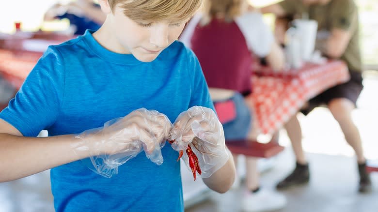 boy holds crawfish with gloves