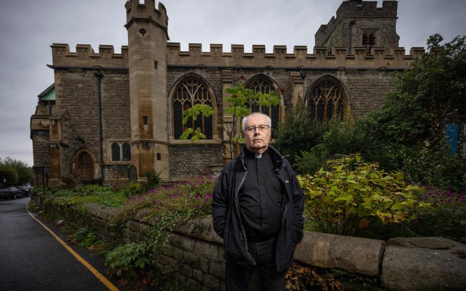 Wearing his priest's collar, Father Brandes poses with the crenellated exterior of the church visible behind him