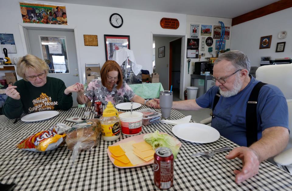 During their lunch break Mary Haigh, left, friend Laura Richie, center, and Larry Haigh, right, of Haigh’s Sugar House Farm in Bellevue pray before eating on Thursday, Feb. 22, 2024.