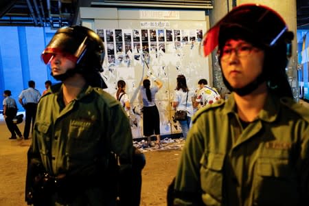 Riot police are seen in front of pro-China supporters as they pull down "Lennon Walls" of anti-government posters and memo outside Yuen Long MTR station in Hong Kong