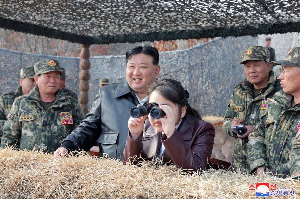 North Korean leader Kim Jong Un's daughter Kim Ju Ae looks through binoculars while standing beside her father and North Korean military personnel.