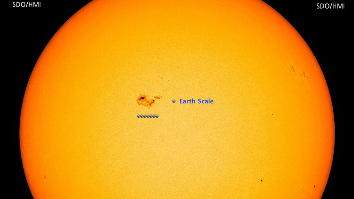  An orange/yelow image of the sun with a sunspot near the center. Seven scale-sized Earths are lined up next to the sunspot to show its enormity.  