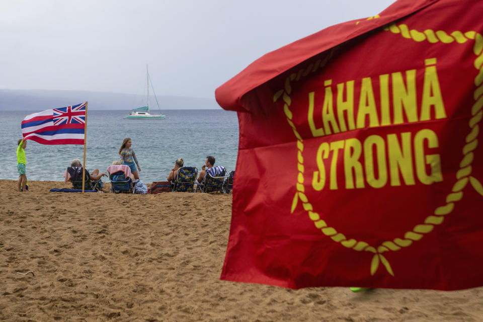 A tourist family sit on the beach next to the Lahaina Strong "Fish-in" on Friday, Dec. 1, 2023, in Lahaina, Hawaii. Lahaina Strong has set up a "Fish-in" to protest living accommodations for those displaced by the Aug. 8, 2023 wildfire, the deadliest U.S. wildfire in more than a century. More than four months after the fire, tensions are growing between those who want to welcome tourists back to provide jobs and those who feel the town isn't ready for a return to tourism. (AP Photo/Ty O'Neil)