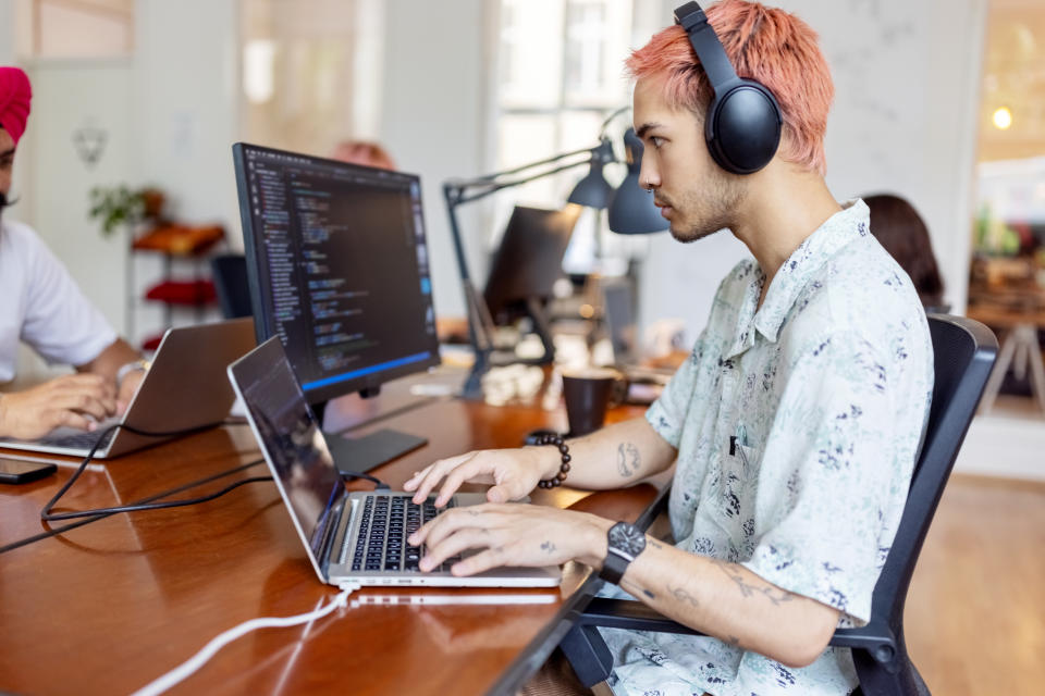 Gen Z man sits in front of a laptop wearing headphones.