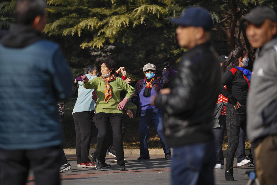 People chat each other, as women, some wearing face masks to help curb the spread of the coronavirus practice social dance at a park in Beijing, Thursday, Nov. 5, 2020. China is suspending entry for most foreign passport holders who reside in Britain, reacting to a new surge of coronavirus cases in the United Kingdom. (AP Photo/Andy Wong)
