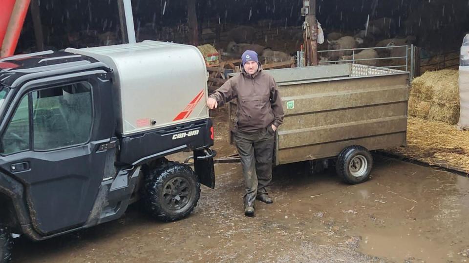 A photo of a farmer in the rain in front of a barn