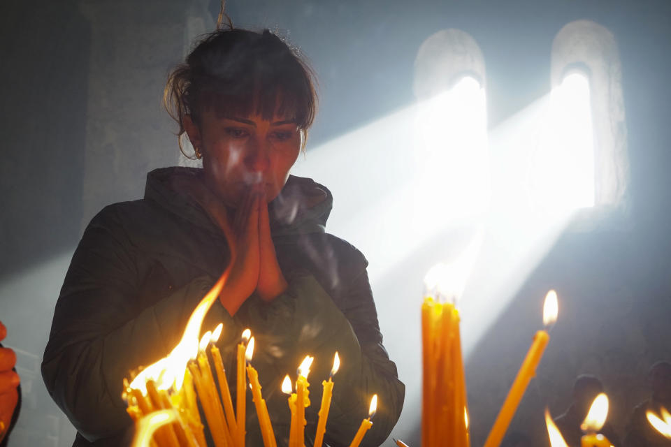 A woman lights candles inside a church of the Dadivank, an Armenian Apostolic Church monastery dating to the 9th century, as ethnic Armenians leave the separatist region of Nagorno-Karabakh to Armenia, Saturday, Nov. 14, 2020. The territory is to be turned over to Azerbaijan on Sunday as part of territorial concessions in an agreement to end six weeks of intense fighting with Armenian forces. Hundreds of thousands of Azeris were displaced by the war that ended in 1994. It is unclear when any civilians might try to settle in Karvachar — which will now be known by its Azeri name Kalbajar — or elsewhere. (AP Photo/Dmitry Lovetsky)