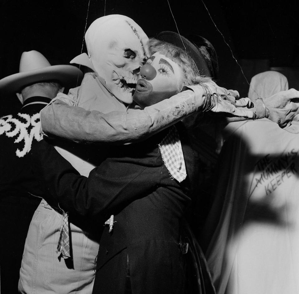 <p>A ghoulish goblin and a painted clown embrace at a Halloween party in 1955. </p>