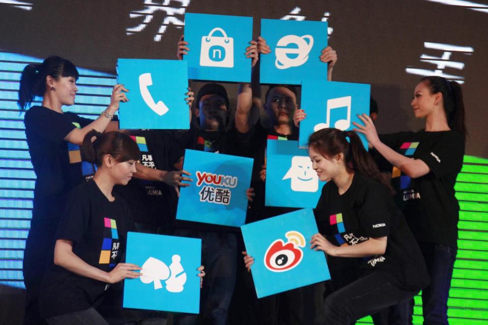 In this March 28, 2012 photo, Chinese performers hold up cards showing the various apps available for online users for shopping and other services at the launch of a mobile phone in Beijing, China. In an abrupt shift, some 81 percent of China’s 618 million Internet users go online via smartphone or tablet, part of a worldwide trend known as the mobile Internet. The services Chinese users flock to are usually privately owned, while the competitors they leave behind belong to the state. Video websites compete with state TV, online financial services draw deposits away from banks and instant messaging apps take revenue from government-owned phone carriers. (AP Photo/Ng Han Guan)