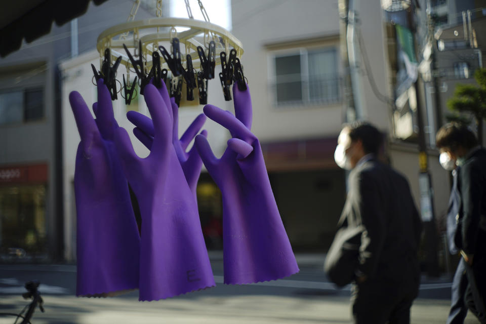 Rubber gloves hang to dry as people wearing protective masks to help curb the spread of the coronavirus walk past in Tokyo Thursday, Jan. 14, 2021. The Japanese capital confirmed more than 1500 new coronavirus cases on Thursday. (AP Photo/Eugene Hoshiko)