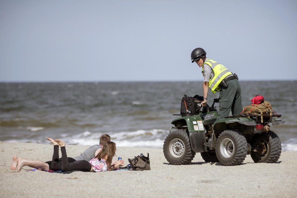 Georgia Department of Natural Resources Law Enforcement Division Corporal Barry Britt, right, enforces Gov. Bryan Kemp's order to open the beaches on Tybee Island, Ga., Saturday, April 4, 2020, allowing people to exercise outside, with social distancing of at least six feet because of the coronavirus outbreak. (Stephen B. Morton/Atlanta Journal-Constitution via AP)