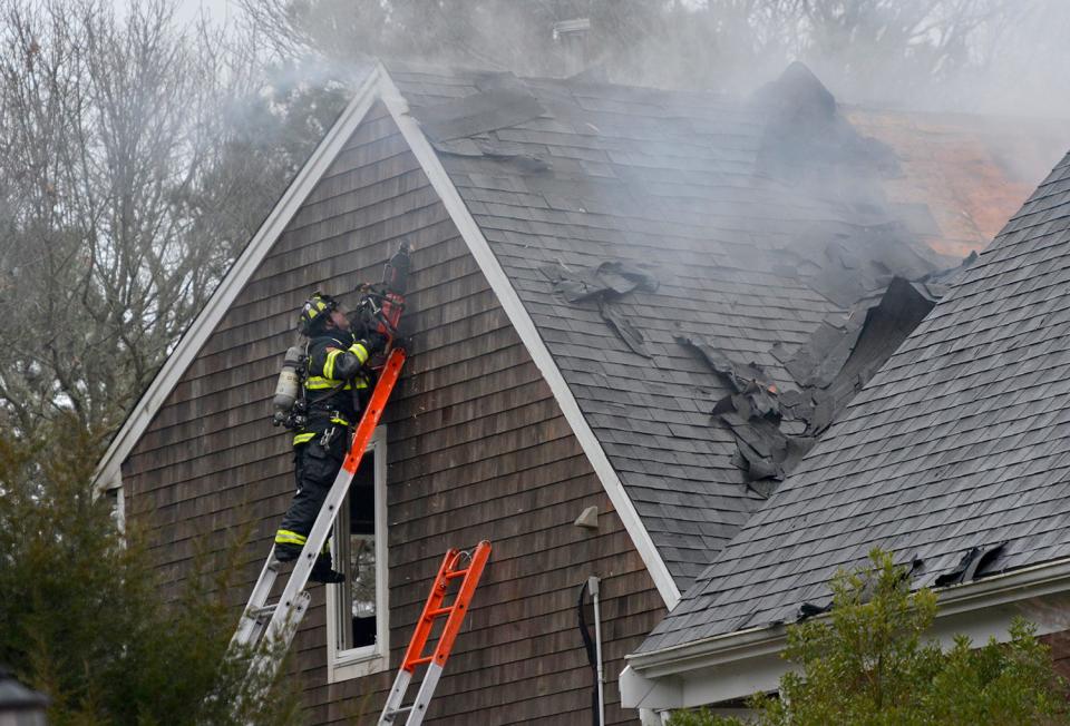 A firefighter uses a chainsaw to open up a wall on the second floor of a home on 22 Rivers Edge Road in Falmouth that caught fire Sunday afternoon. Falmouth and other area firefighters responded to the scene.