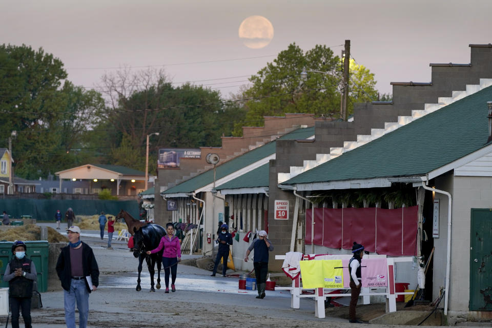 Workers tend to horses in barns as the full moon sets during morning workouts at Churchill Downs Tuesday, April 27, 2021, in Louisville, Ky. The 147th running of the Kentucky Derby is scheduled for Saturday, May 1. (AP Photo/Charlie Riedel)