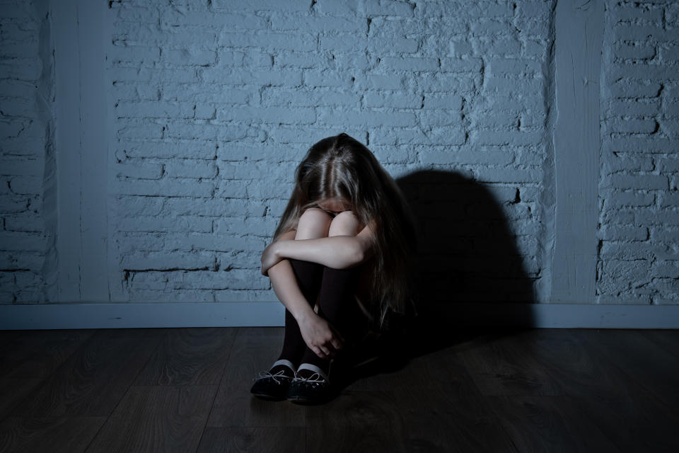 A young girl crouched against the wall. 