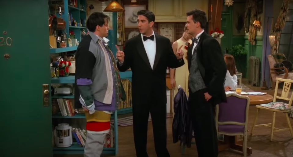 Ross stands between a fighting Chandler and Joey, the latter of whom is wearing all of Chandler's clothes