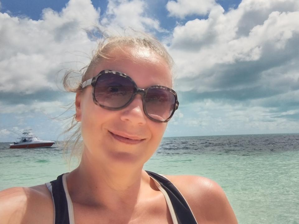 Woman wearing dark sunglasses smiling for a selfie in front of the ocean