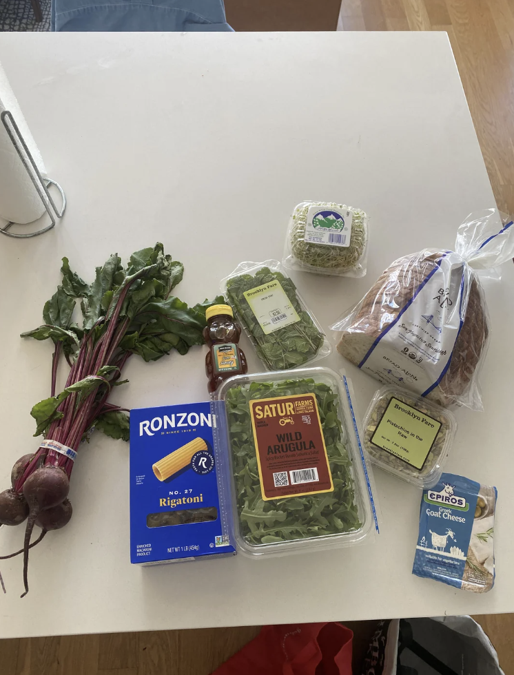 A table displaying fresh beets, rigatoni pasta, wild arugula, goat cheese, bread, honey, and Greek cheese