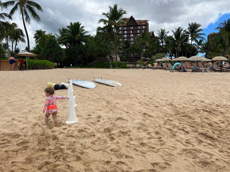 A toddler on the sand of the beach holding onto a white cone.