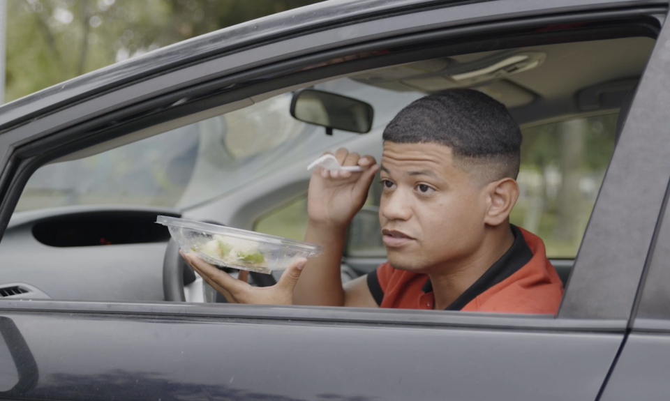 gadiel in a car's driver's seat holding a salad