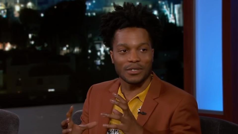 Actor Jermaine Fowler giving an interview in tan suit and yellow shirt