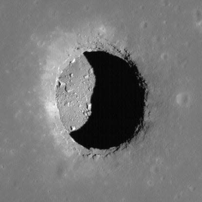 close up of a pit on the moon showing a shadowed region on the pit's bottom with loose debris lining the inside