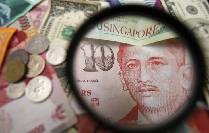 Singapore currency notes are seen through a magnifying glass among other currencies in this photo illustration taken in Singapore April 12, 2013. REUTERS/Edgar Su
